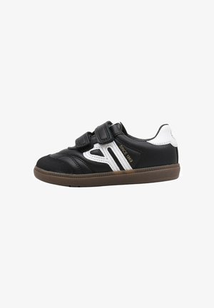 Zapatilla deportiva negra con dos correas de velcro, acentos blancos en los laterales, parte superior negra texturizada y suela de goma marrón. Adecuada para deportes y uso casual.