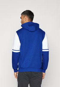 Königsblauer Hoodie mit weißen Ärmeln, gerippten Bündchen und Kapuze mit Kordelzug. Verfügt über horizontale Streifen an den Ärmeln und einen lässigen Schnitt.