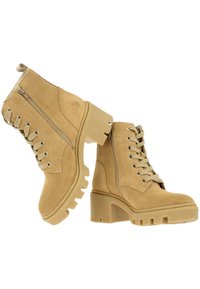 Botines de ante beige con un tacón grueso, parte delantera con cordones y cremallera lateral, que presentan una suela texturizada y costuras reforzadas.