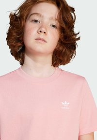T-shirt en coton rose avec un col rond et des manches courtes, arborant un logo Adidas blanc sur la poitrine gauche.