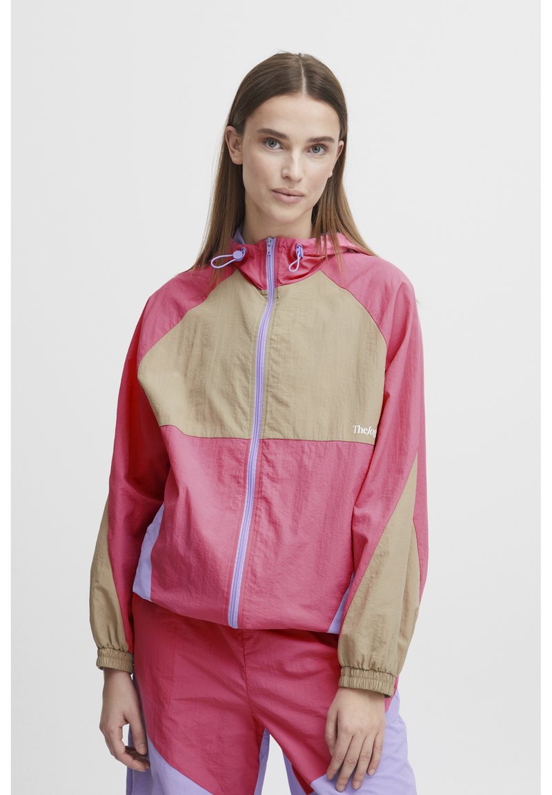 Rompevientos colorido en rosa, beige y lavanda. Presenta una capucha, cremallera frontal, puños elásticos y detalle de logo. Tejido ligero y texturizado.