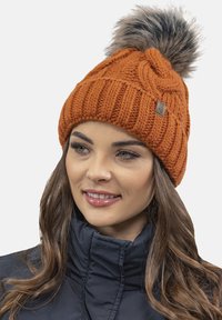 Berretto lavorato a maglia arancione con un motivo testurizzato e bordo a coste, dotato di un pompon in pelliccia sintetica sulla parte superiore. Piccolo etichetta con il marchio sul lato.