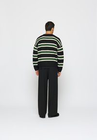 Liela izmēra melna džemperis ar zaļām un baltām svītrām, ar apaļu kakla izgriezumu un ribotām aprocēm, apvienots ar brīviem melniem biksēm.