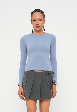 Lichtblauw long-sleeve shirt met een ronde halslijn, gecombineerd met een donkergrijze plissérok met zijveters. Soepele stoftextuur.