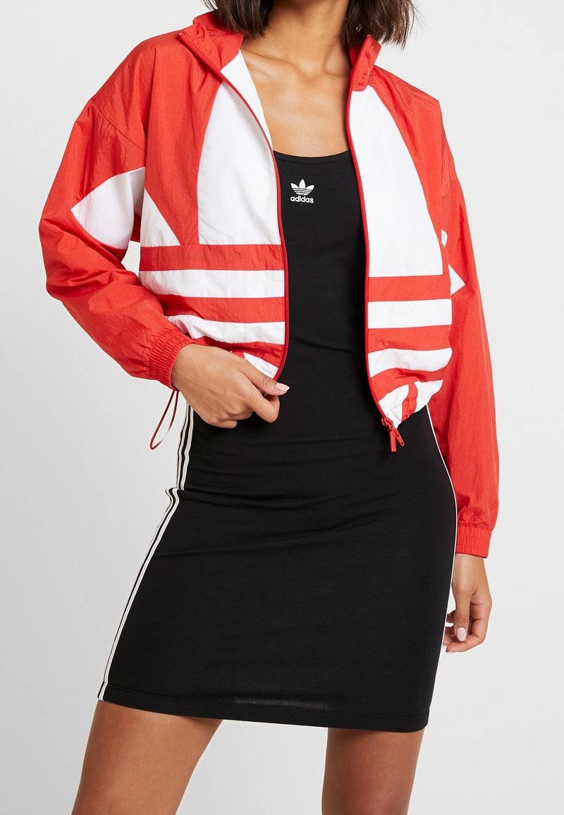 Röd och vit vindjacka med elastiska muddlar och dragkedja fram, bärs över en svart klänning med ärmlös design som har vita sidostreck.