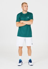 Herrarnas träningskläder bestående av en teal kortärmad tröja och vita shorts. Tröjan har en subtil logotyp; shortsen har sidostreck och logotypdetaljer.