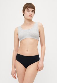 Harmaa puuvillainen croptop, jossa on neliönmuotoinen pääntie, yhdistetty mustiin korkeavyötäröisiin alusvaatteisiin. Sujuva tekstuuri, ei näkyviä kuvioita tai metalliosia.