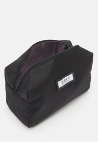 Zwarte stoffen make-up tas met een rechthoekige vorm, gladde textuur, bovenste ritssluiting en een klein wit label met de merknaam.