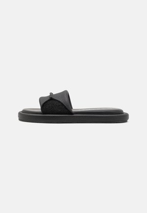 Sort slip-on sandal med polstret sål og tekstureret bred rem, vist i sideprofil på hvid baggrund.