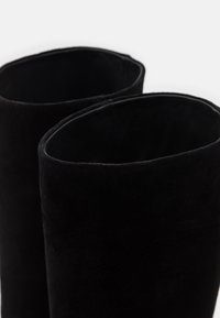 Bottines en daim noir avec un dessus légèrement incurvé, présentant une texture douce et un design minimaliste, mettant en valeur la finition lisse et mate.