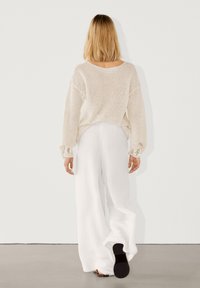 Flødefarvet, løsstrikket sweater kombineret med hvide bukser med vide ben. Bemærkelsesværdige detaljer inkluderer teksturerede ærmer og en afslappet pasform.