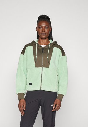 Light green fleece jacket with a brown hood and accents. Features a zip closure, side pockets, and a boxy fit. Smooth texture.