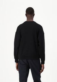 Felpa nera con vestibilità comoda, maniche lunghe e polsini a coste. Texture liscia, design minimalista e senza motivi o logo visibili.