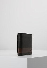 Portefeuille en cuir noir avec une bande d'accent en cuir marron, présentant un design élégant et minimaliste avec des détails de couture distincts.