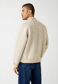 Crème-kleurige sweatshirt met een textuurafwerking, geribbelde kraag en manchetten, en een cropped ontwerp, gedragen over donkere jeans.