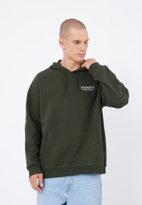 Sweat à capuche vert avec cordon de serrage, poche avant et logo en texte blanc « BALANCE » sur la poitrine. Tissu doux avec des poignets et un ourlet côtelés.