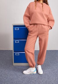 Felpa rosa e pantaloni jogger abbinati, realizzati in tessuto morbido. Presentano polsini elastici e vita con cordino. Indossati con sneakers bianche.