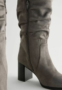 Graue Wildleder-Stiefel bis zum Knie mit quadratischem hohen Absatz, Reißverschluss an der Seite und weichem, gerafftem Texturdetail.