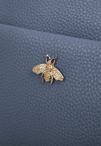 Navyblauwe gestructureerde leren tas met een gouden bij-vormige versiering met gedetailleerde vleugels en lichaam, die visuele interesse aan het ontwerp toevoegt.