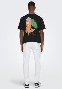 Black t-shirt featuring a cartoon carrot wearing a blue hat and holding a skateboard, accompanied by green plant accents. White pants visible.