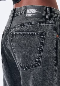 Jeans in denim neri con una finitura sbiadita. Presentano cuciture a contrasto, due tasche posteriori e una toppa in pelle con logo in vita.