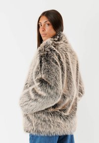 Giacca in pelliccia ecologica in tonalità di grigio e beige, caratterizzata da una consistenza spessa e morbida, vestibilità rilassata e colletto alto.