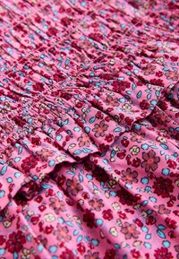 Rózsaszín anyag piros, kék és bézs virágmintával, gyűrt és ráncolt varrással díszítve.