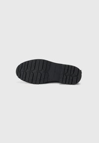 Suela de zapato de goma negra con surcos profundos y la marca "Tommy Hilfiger" grabada en el centro, tamaño 37 visible.