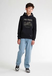 Hanorac negru cu imprimeu grafic de motocicletă, blugi din denim deschis la culoare și adidași negri cu accente albe. Croială casual, manșete striate.