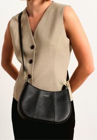 Borsa a tracolla in pelle nera con design curvato, caratterizzata da una superficie testurizzata, hardware dorato e un logo discreto sul frontale.