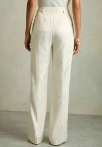 Pantaloni crema su misura con vita alta e gamba dritta. Presentano discrete tasche sul retro e un tessuto morbido e testurizzato.