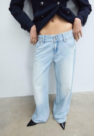 Persona che indossa jeans a vita alta azzurri con gambe larghe, scarpe nere con punta, e una giacca doppiopetto corta blu navy che lascia scoperto l'addome.