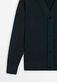 Donkerblauwe geribbelde cardigan met een V-hals, zes zwarte knoopjes en lange mouwen. Heeft een gestructureerde stof en een rechte snit aan de zoom.