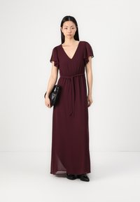 Burgundy maxi dress with a V-neck, short flutter sleeves, cinched waist, and a tied belt. Smooth, flowing fabric with a layered texture.