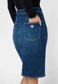 Džinsinė pieštuko sijonas su aukštu juosmeniu, šonine kišene, mėlynu atspalviu, subtiliu blukimu ir trikampiu logotipo pažymėjimu ant galinės kišenės.