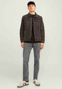 Črni denim jakna čez črno majico, kombinirana s sivimi jeans hlačami in bež supergami. Obleka ima sproščen dizajn in klasičen kroj.