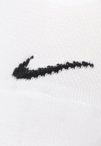 Hvid sportssok med tekstureret strik. Har et fremtrædende sort Nike swoosh-logo på den ydre side.
