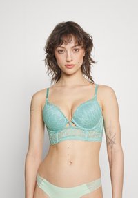 Reggiseno in pizzo color turchese con scollatura profonda, supporto con ferretto e decorativa apertura a chiave frontale. Bordo in pizzo coordinato sul sottobande e slip abbinati.