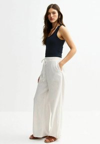 Marine tanktop gecombineerd met witte, gestreepte, wijde broek met een trekkoord in de taille en zijzakken. Bruine, gespsandalen maken de look compleet.