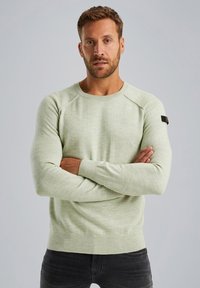 Hellgrüner gestrickter Pullover mit gerippten Bündchen und Saum. Verfügt über einen runden Halsausschnitt und eine dezente Textur. Enthält ein schwarzes Logo-Patch am Ärmeln.