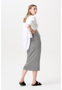 Witte cropped shirt met opgerolde mouwen, gecombineerd met een geribbelde grijze midi-rok. Zwarte sandalen met een kurken zool maken de outfit compleet.