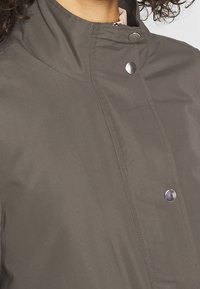 Grå vattentät jacka med hög krage, silverfärgade tryckknappar och slät yta. En nödvändighet f ör skydd mot väderelement.