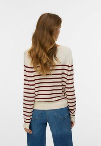 Cream and burgundy striped sweater with long sleeves, ribbed hem, and relaxed fit, paired with blue high-waisted jeans.