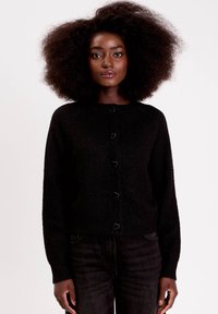 Cardigan noir en fil doux avec un col rond, orné de boutons en forme de cœur et de manches longues, associé à du denim foncé.