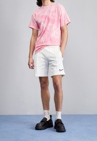 Pink tie-dye short-sleeve T-shirt, white athletic shorts with black Nike logo, and black slip-on shoes with a thick sole. Light background.