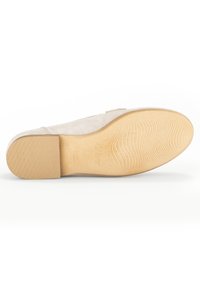 Beige suede shoe with a smooth texture, rubber sole featuring ridges for grip, and stitched detailing along the side.