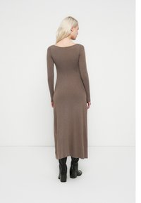 Vestido ajustado de manga larga con tejido acanalado en color marrón. Presenta un escote redondeado en la espalda y un dobladillo recto, combinado con botas negras hasta la rodilla.