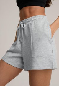 Shorts en mélange de coton gris clair avec une taille élastique et un cordon de serrage, comportant des poches latérales et une coupe décontractée. Texture lisse.