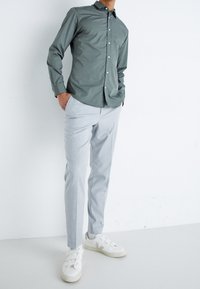 Camicia verde con bottoni, pantaloni grigi chiari su misura, sneaker bianche con un design a strap. Tessuto liscio e silhouette slim fit.