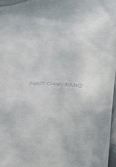 Γκρι ύφασμα με λεπτό κεντητό κείμενο "Feng Chen Wang" στο κέντρο, που δείχνει υφή και λεπτομέρειες υλικού.